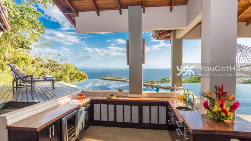 Amazing covered swim-up bar in pool, view from the deck with wine cooler, sink, tropical flowers and huge ocean view behind the pool.
