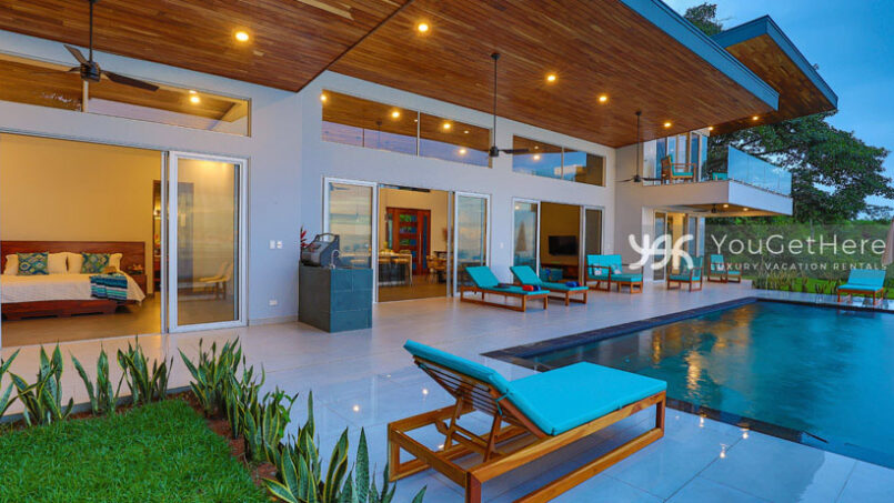 Large pool deck full of lounges and chairs, home features large sliders that open onto pool deck.