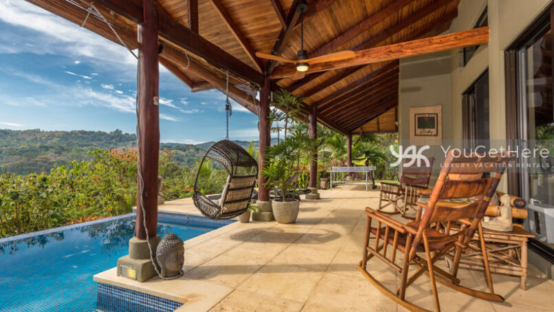 Covered outdoor patio space with rocking chairs and hanging swing chairs at the pool of Villa Koora.
