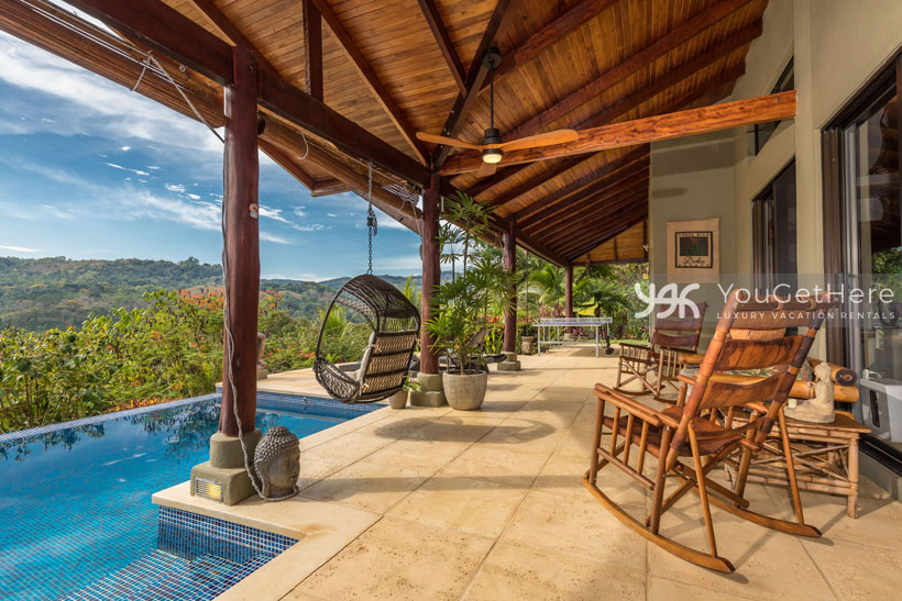 Covered outdoor patio space with rocking chairs and hanging swing chairs at the pool of Villa Koora.