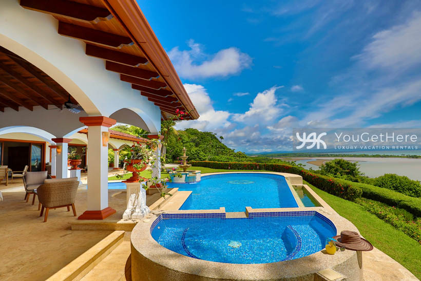 Vista Encanto Costa Rica full view of pool and tub surrounded by manicured hedges and full ocean views on a sunny day.