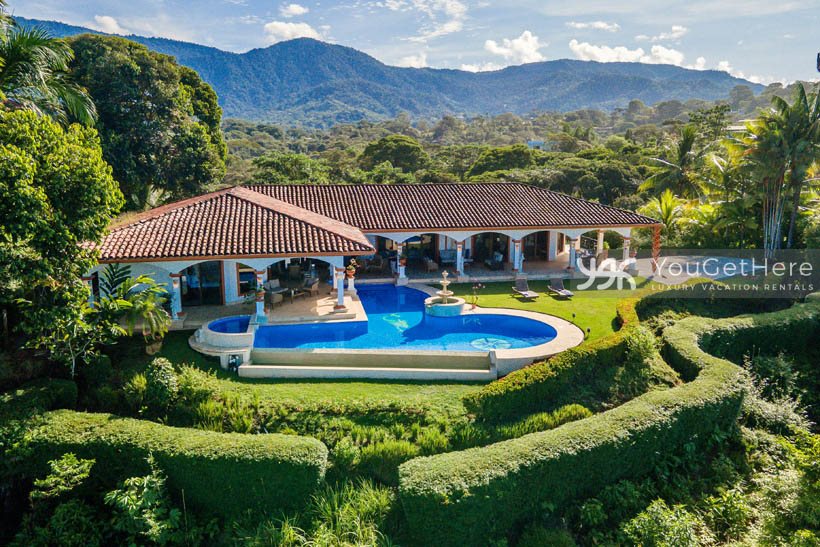 Aerial view of Vista Encanto Costa Rica with huge swimming pool and lots of green grass enclosed by manicured hedges.