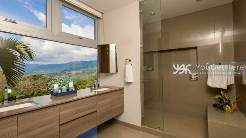 Massive primary bathroom with sleek modern design and full walled windows overlooking stunning jungle views.