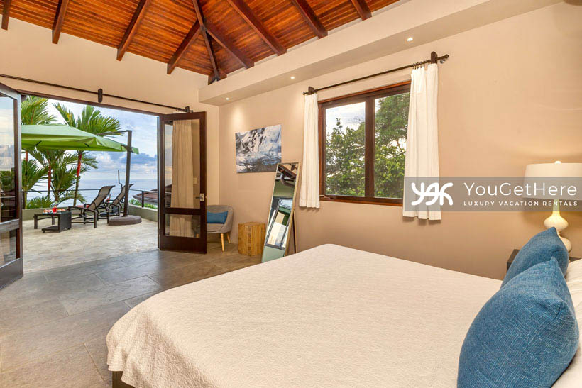 Jade House Costa Rica relaxing guest bedroom with french doors leading out to ocean view deck and covered lounge chair seating.