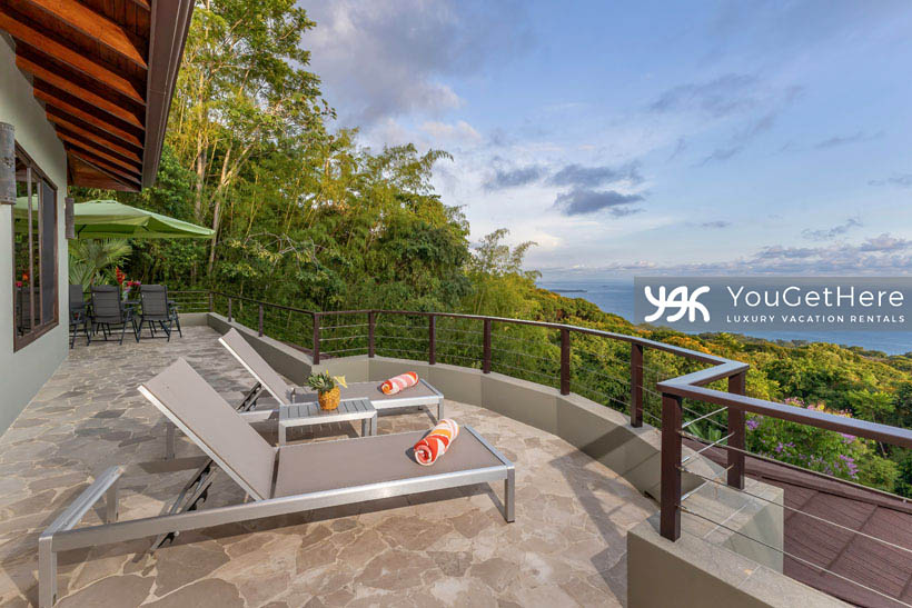 Jade House Costa Rica upstairs deck lounge chairs and large dining table with umbrella, both featuring massive ocean views over the three pools below.