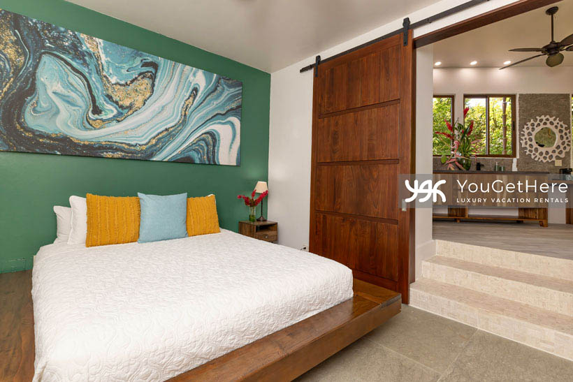Jade House Costa Rica sleek and modern interior decor with king-bed set into custom wood platform, ocean and sand color art and beautiful natural stone flooring.