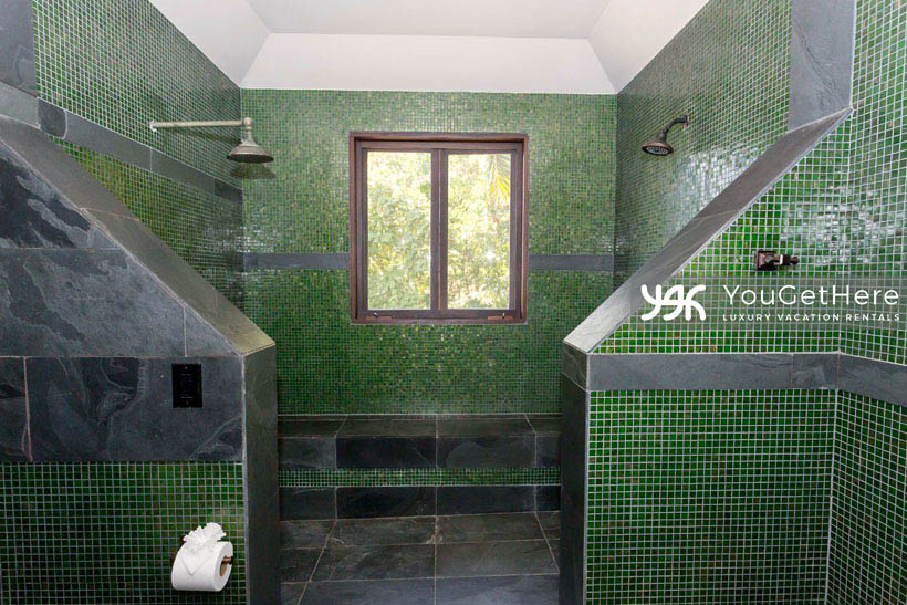 Jade house Costa Rica massive walk-in shower featuring dark green tiling and black stone details, dual opposing shower heads and huge stone bench seating next to window with fresh jungle view.