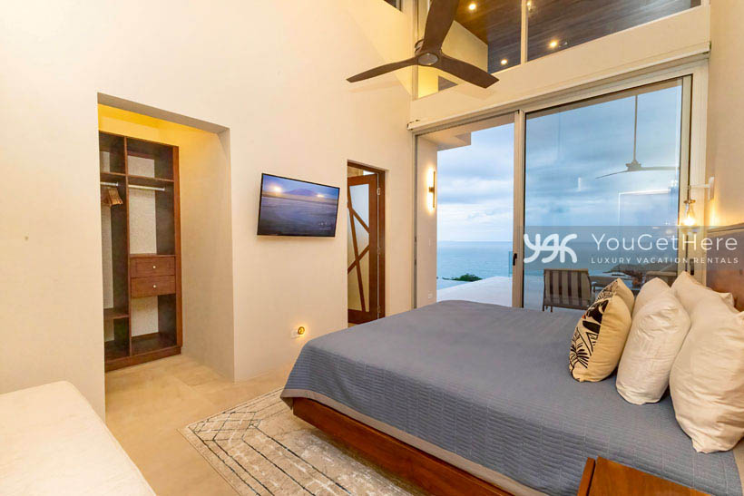 Accommodating guest suite with wall-mounted television, in-suite bathroom, overhead ceiling fans and panoramic ocean and sky views.