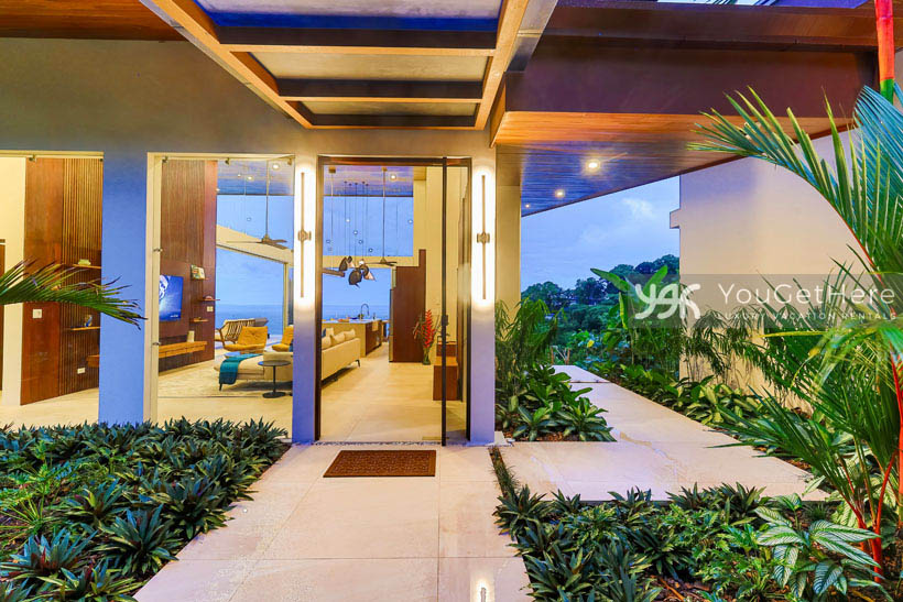 Tropical landscaping surrounding beautiful entry way with glass window walls and full ocean view.